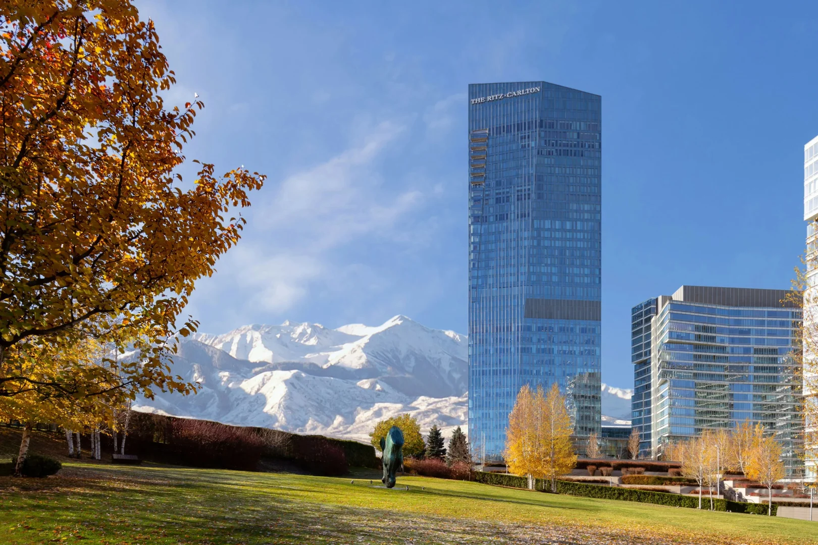 Башня Esentai Tower с вывеской The Ritz-Carlton на фоне снежных гор