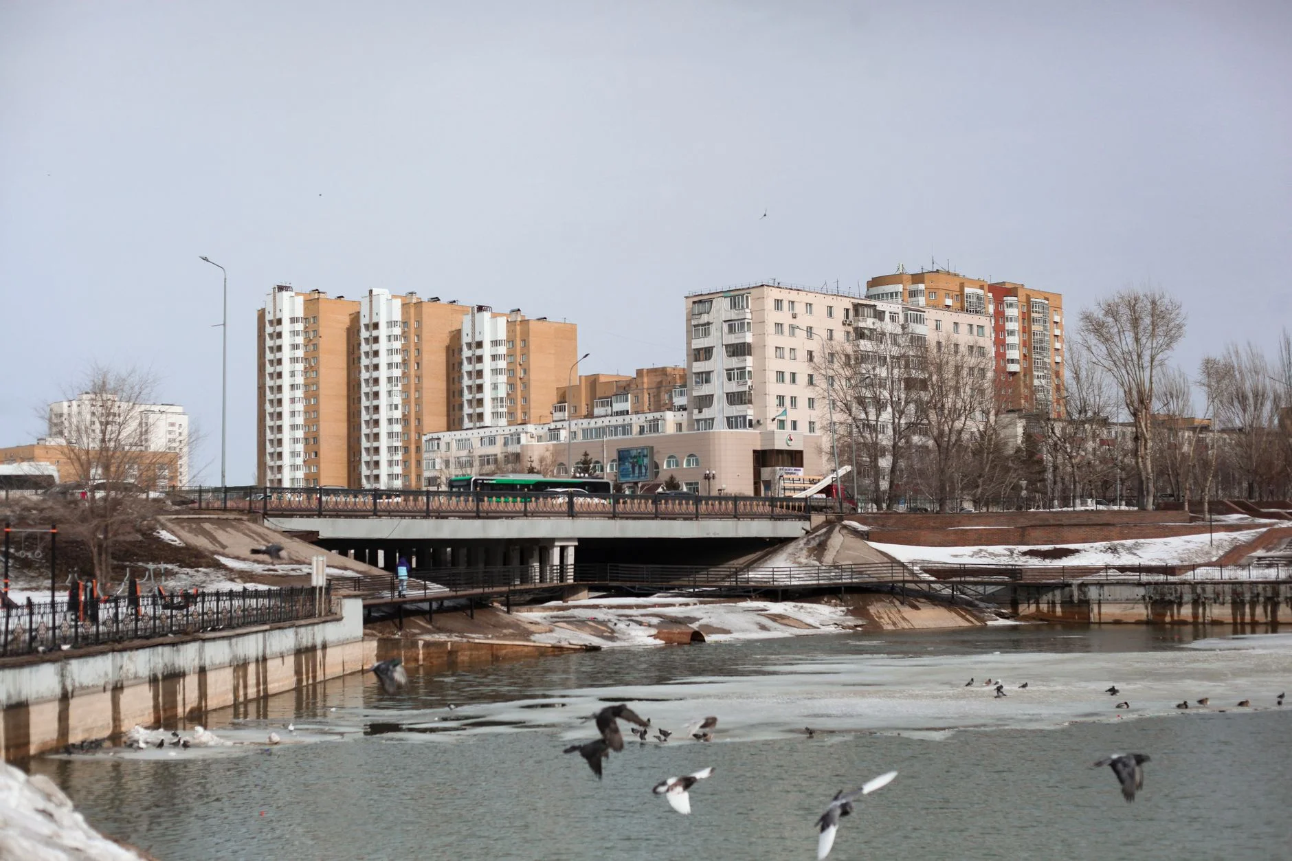 Жилые дома у реки в Астане, мост и лёд на воде